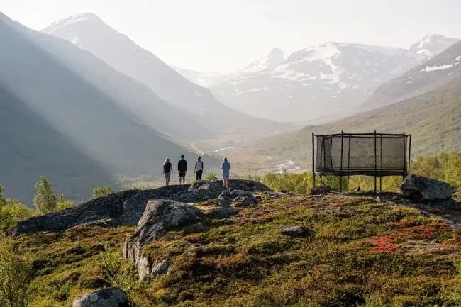 People standing next to a trampoline in a mountain landscape